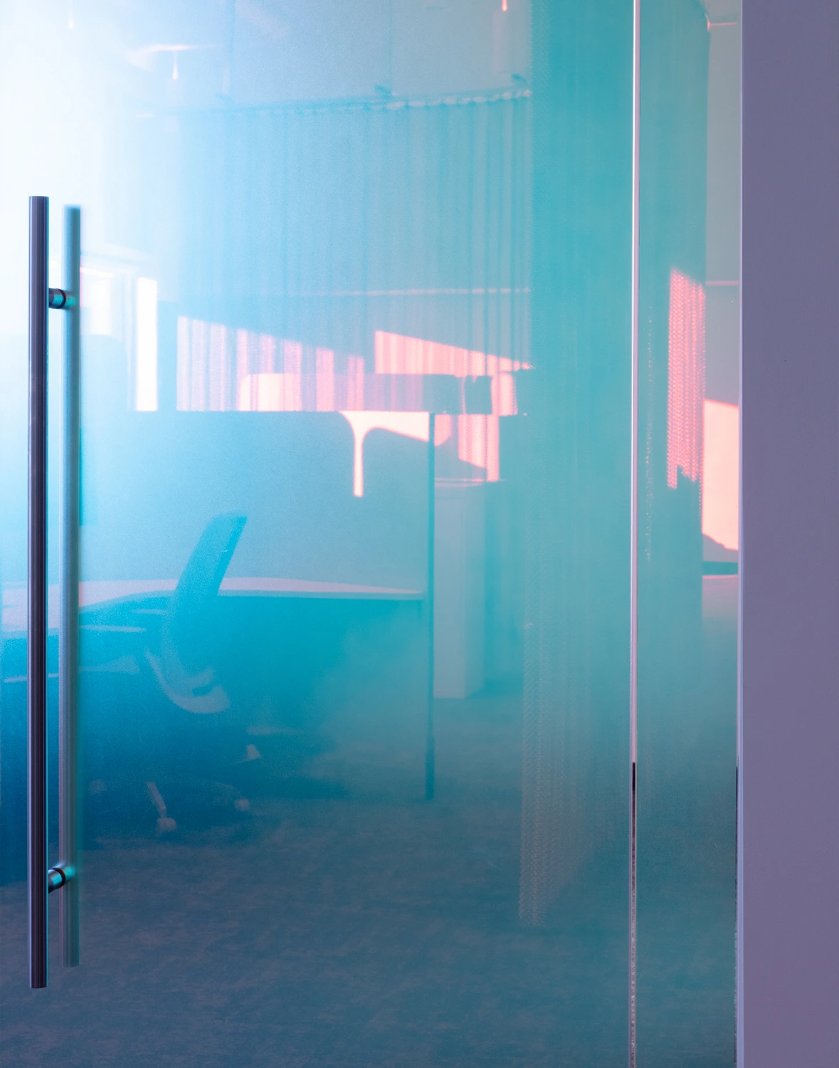 Interior view looking through a glass partition displaying vibrant pink and blue iridescent light reflections in a contemporary office setting.