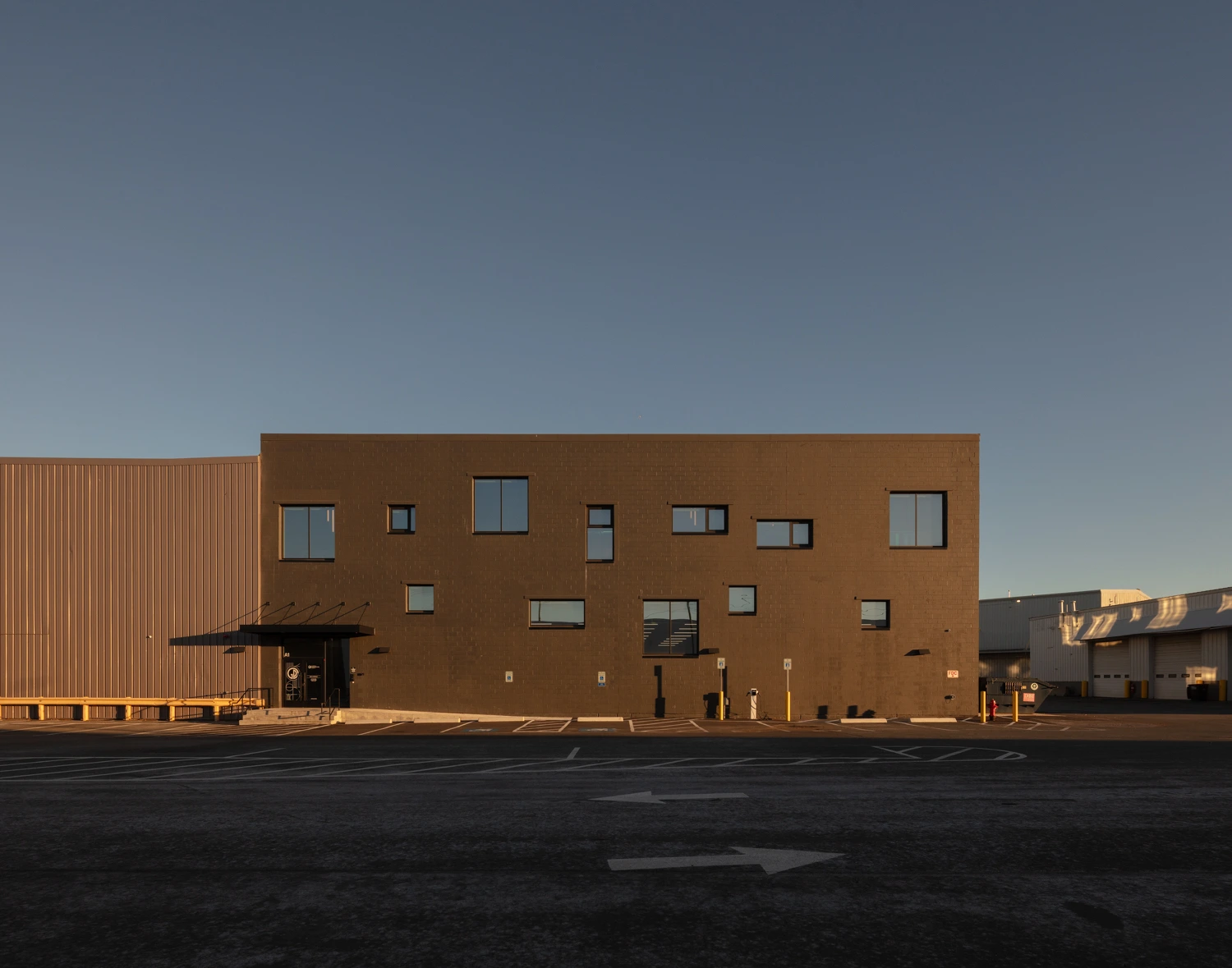 Architectural photograph of a modern, minimalist rectangular building exterior at dusk, featuring warm lighting glowing from square windows.