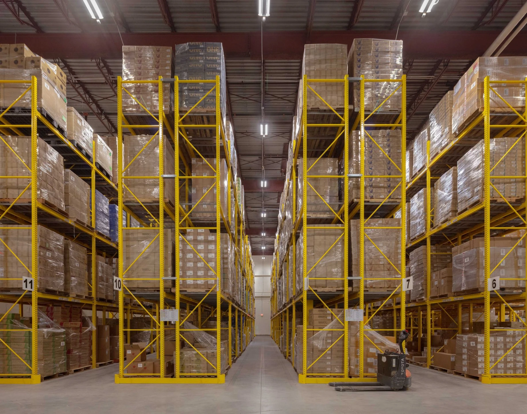 Wide-angle view of a spacious commercial warehouse interior with tall, organized yellow industrial pallet racks for product distribution.