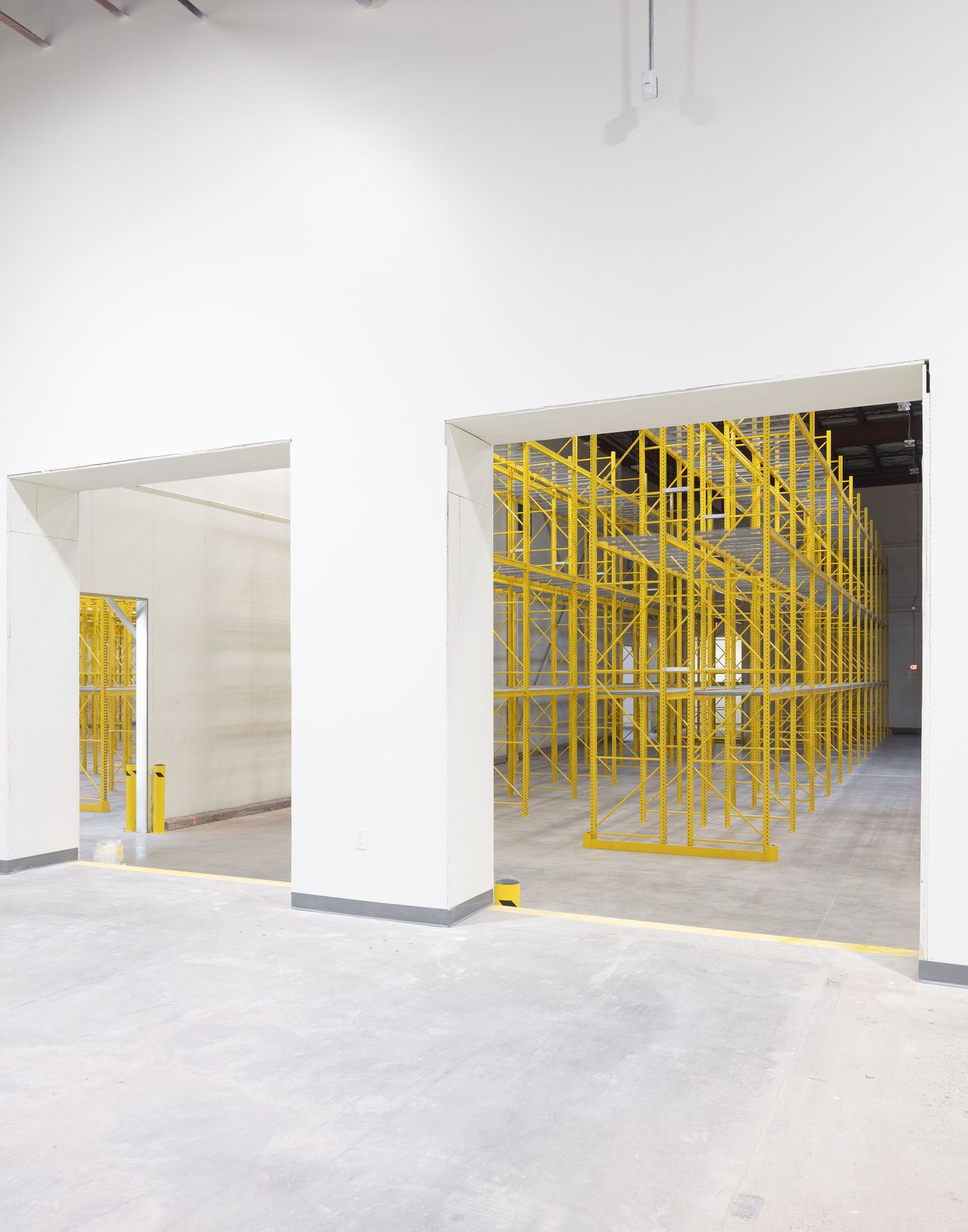 Interior view of a clean, white industrial or manufacturing space during a buildout phase, featuring yellow safety racking.