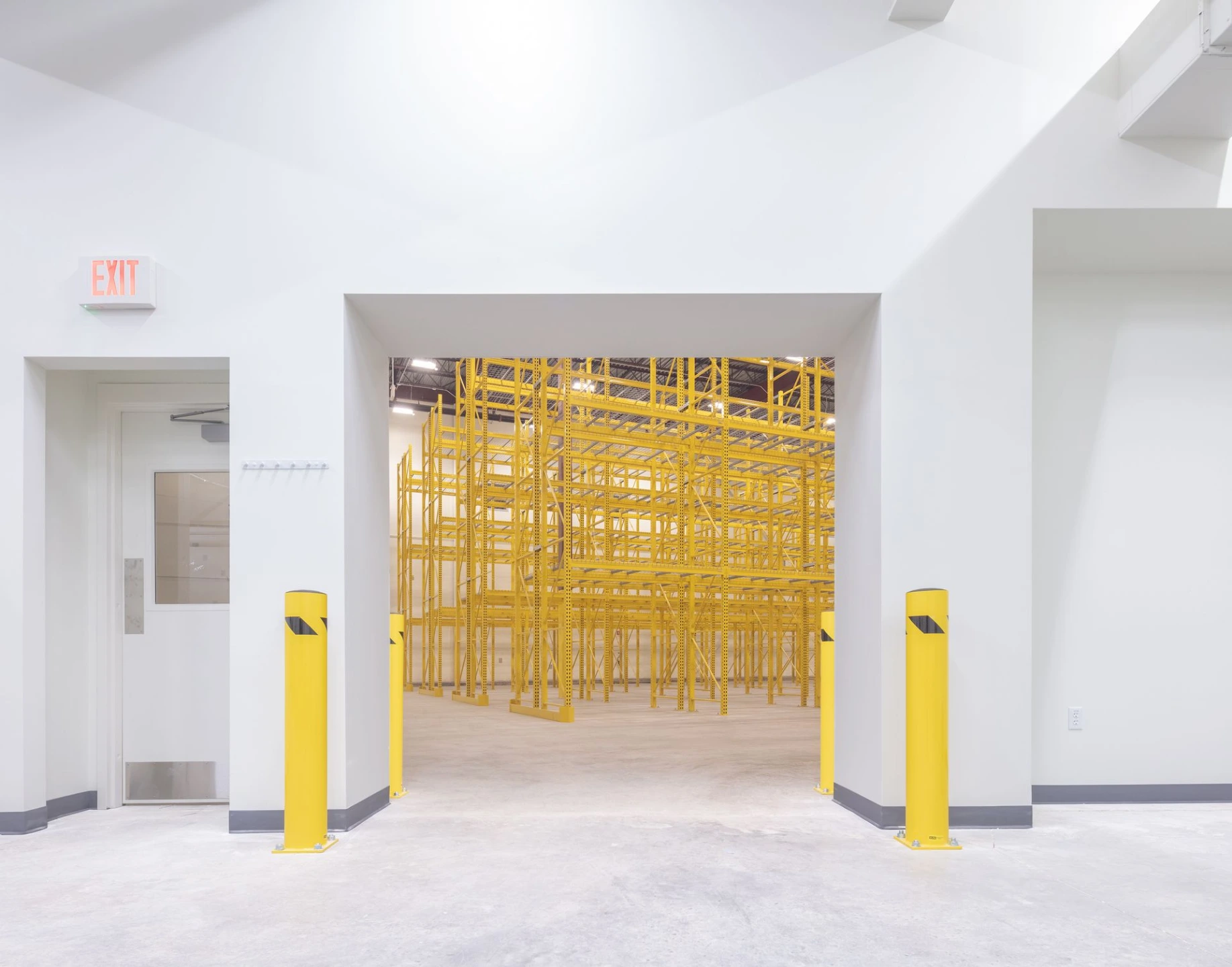 View through a clean, white internal doorway looking directly into a warehouse zone filled with yellow industrial pallet racks.