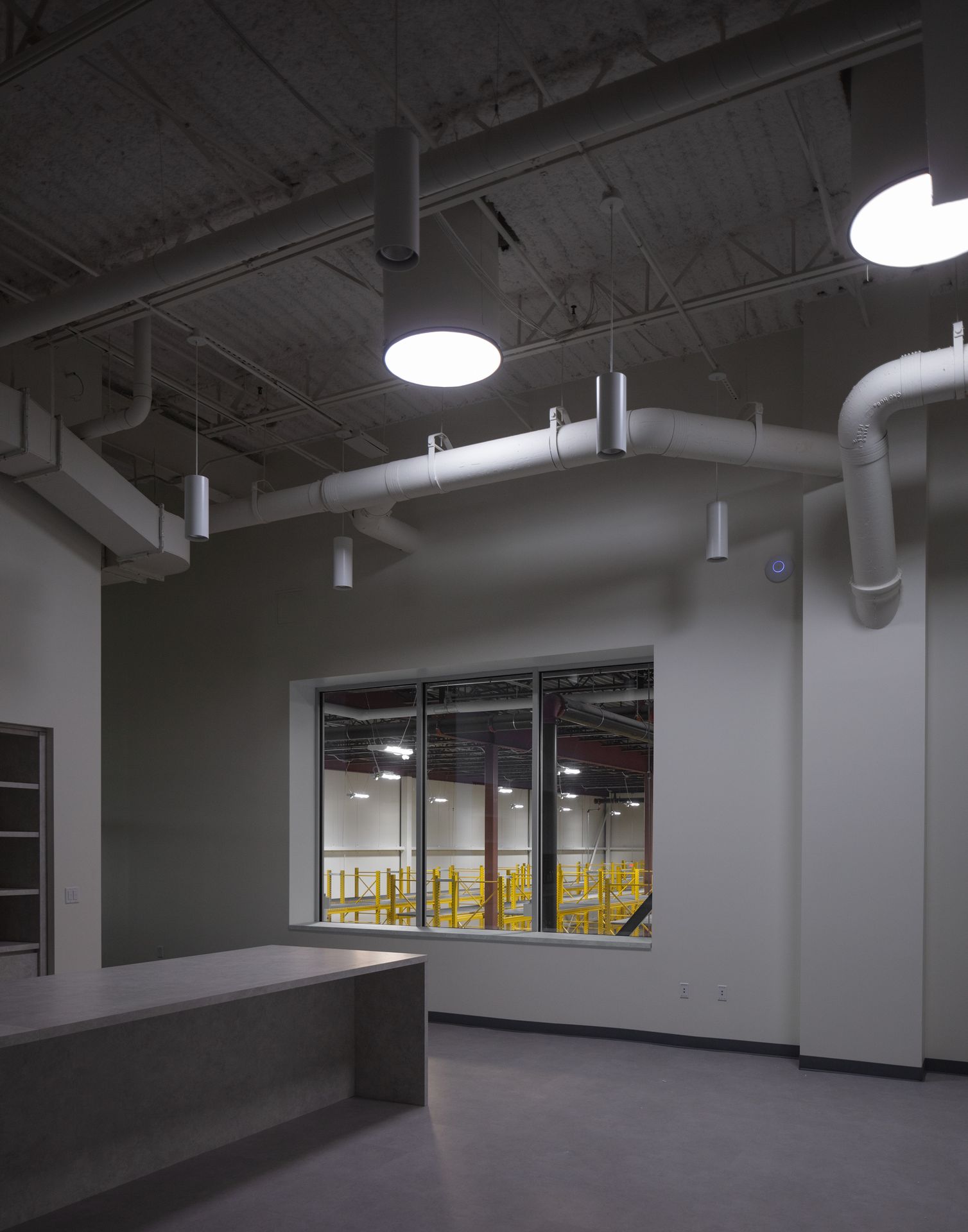 Industrial interior shot focusing on exposed silver ductwork, piping, and round overhead light fixtures against a dark ceiling.