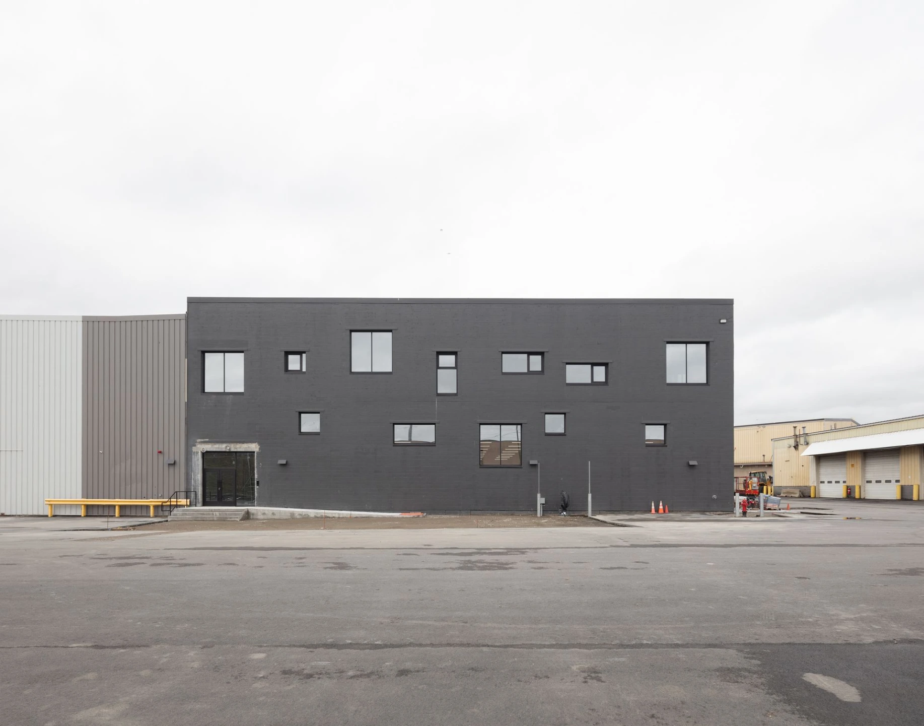 Architectural photograph of a long, dark grey rectangular modern building facade with small square windows under a cloudy sky.