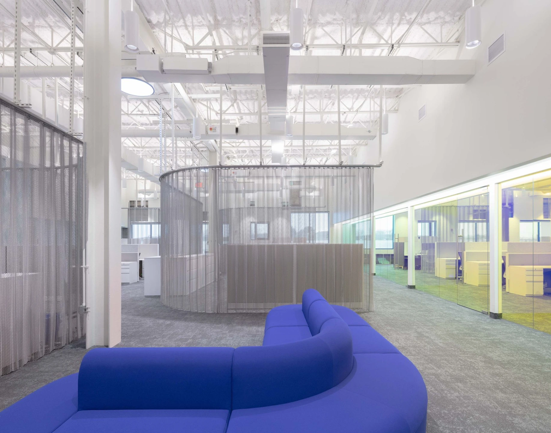 Interior view of a clean industrial or manufacturing buildout space featuring a bright blue modular couch on the left and safety scaffolding in the background.