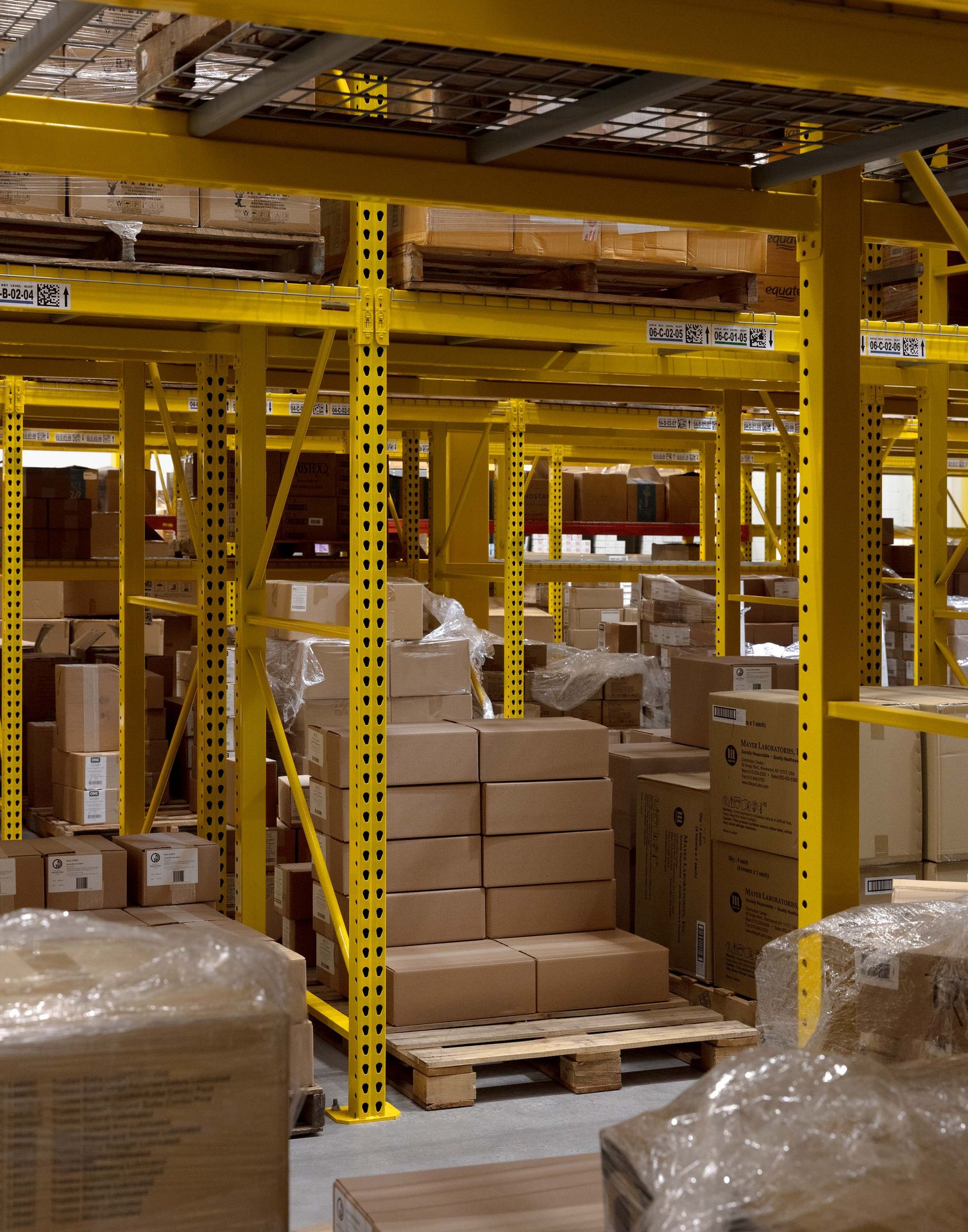 Wide shot of a spacious commercial warehouse interior featuring tall, yellow industrial pallet racks loaded with inventory boxes.