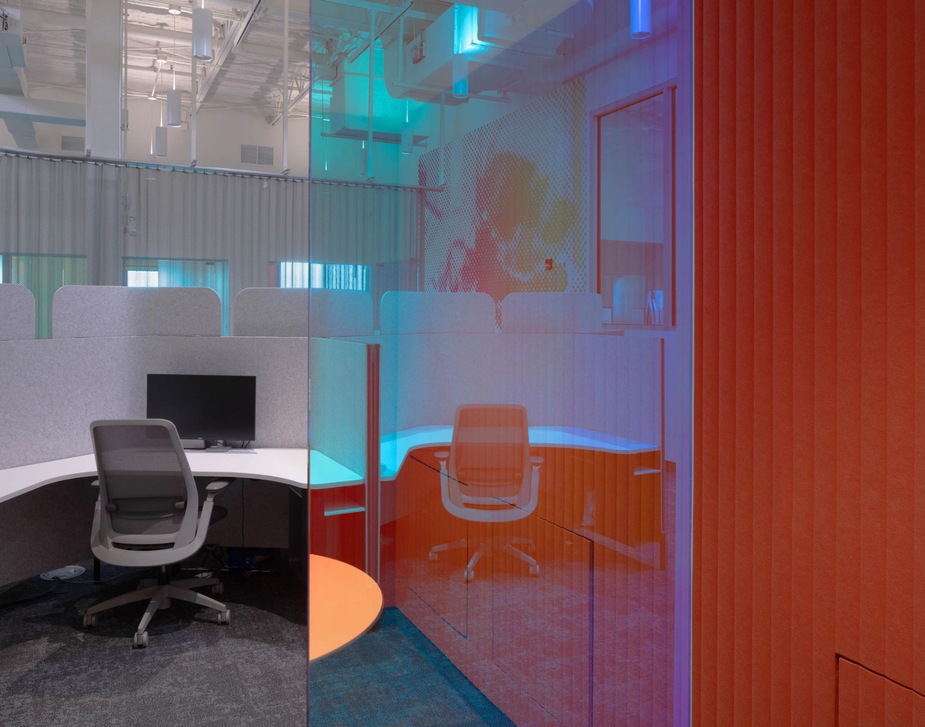 Interior view of a contemporary office space with glass partitions reflecting soft pink and blue ambient lighting.