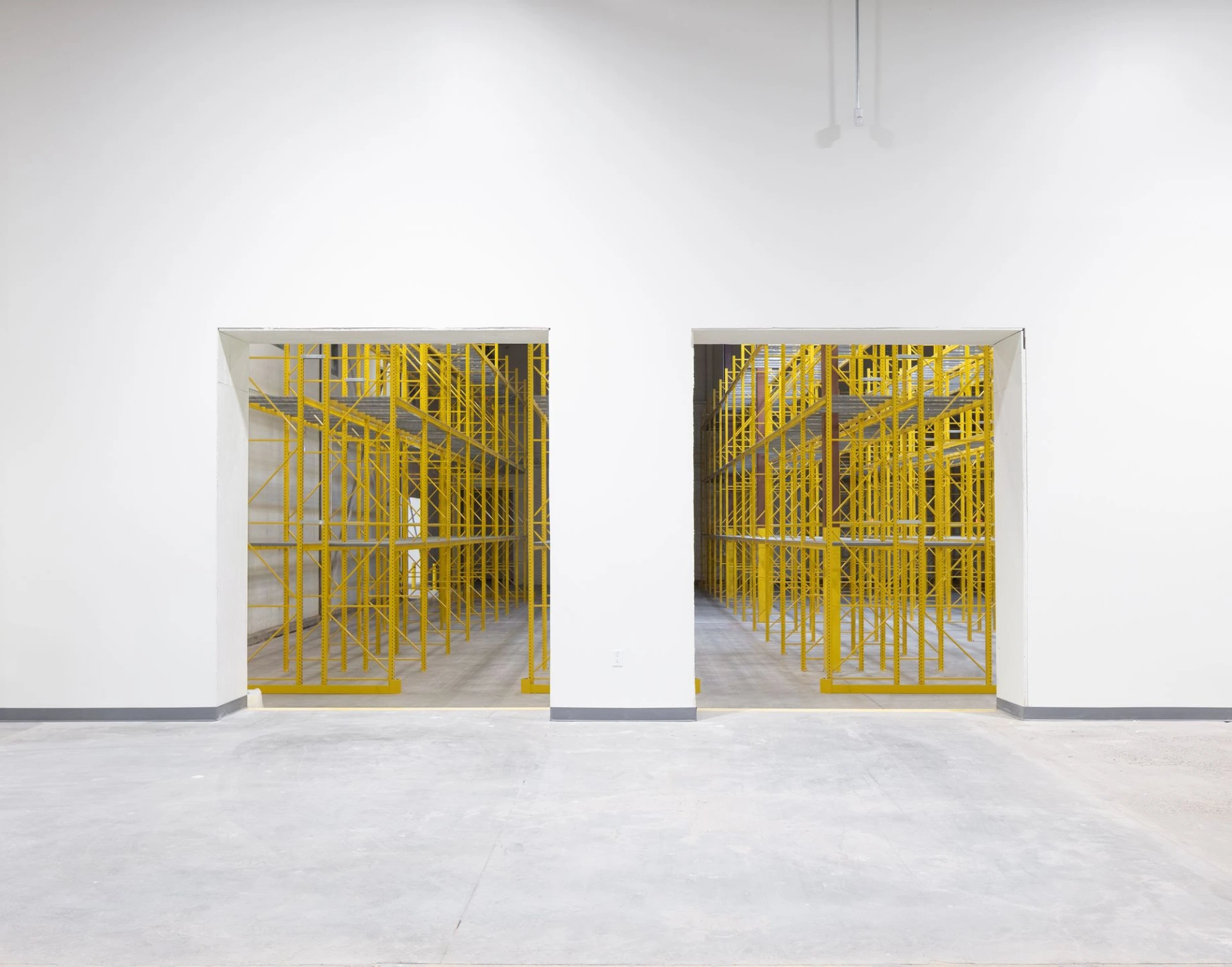 A clean, wide-open industrial warehouse interior featuring two open roll-up doors revealing bright yellow storage racks inside.