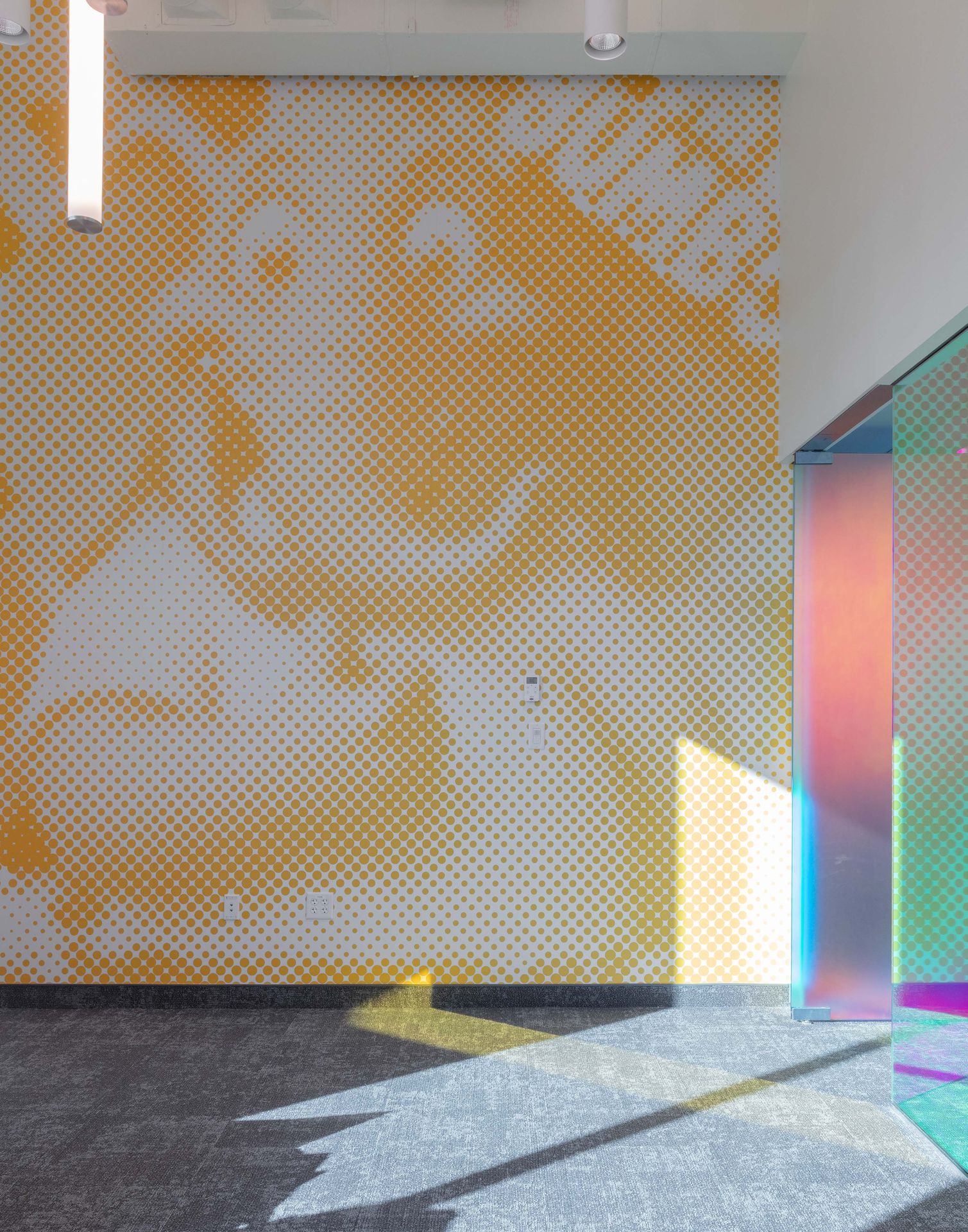 Close-up of an interior wall decorated with a textured, golden geometric honeycomb pattern catching bright natural sunlight and creating colorful reflections.