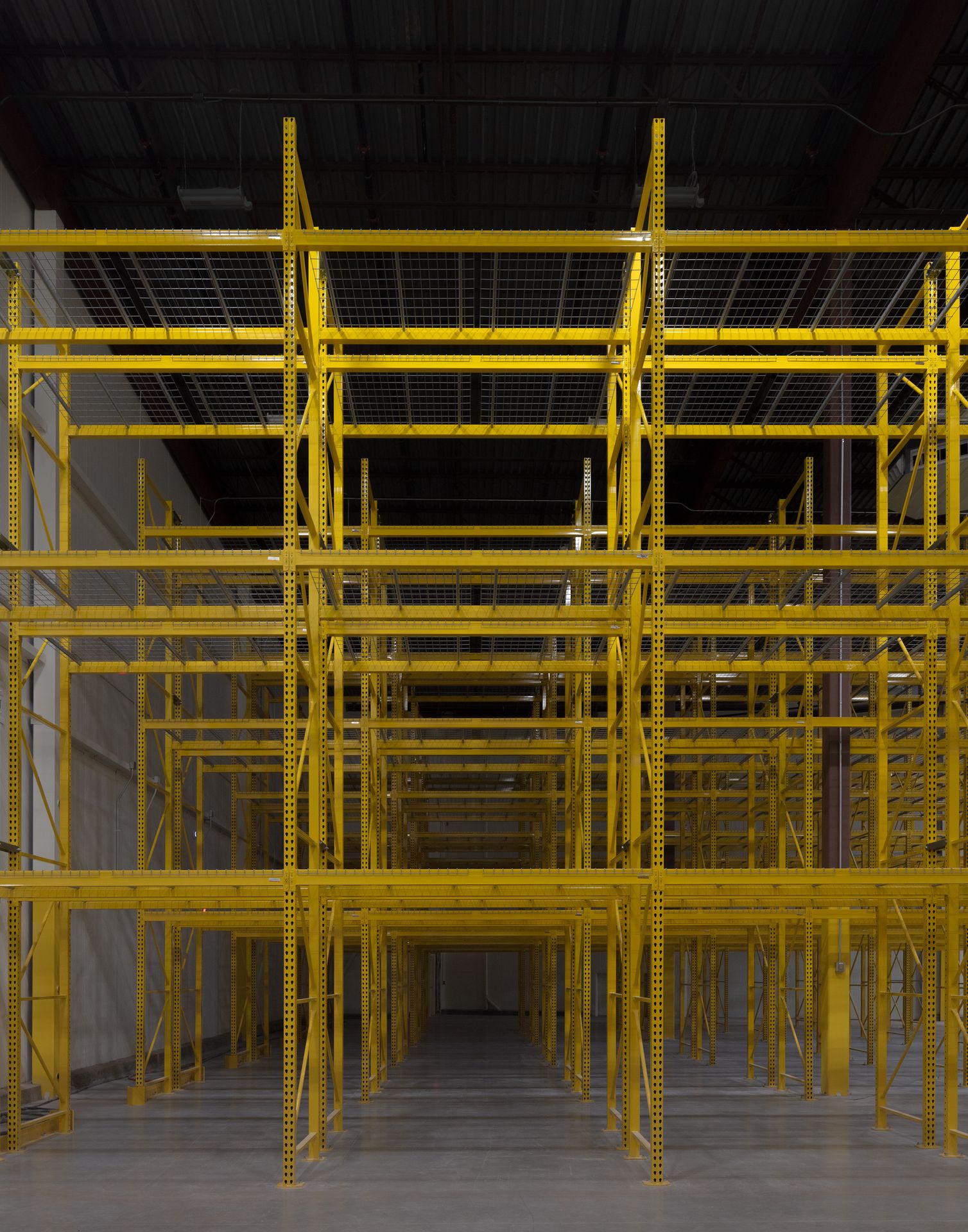 Symmetrical, front-facing view looking down an empty aisle of tall, yellow industrial storage racks.