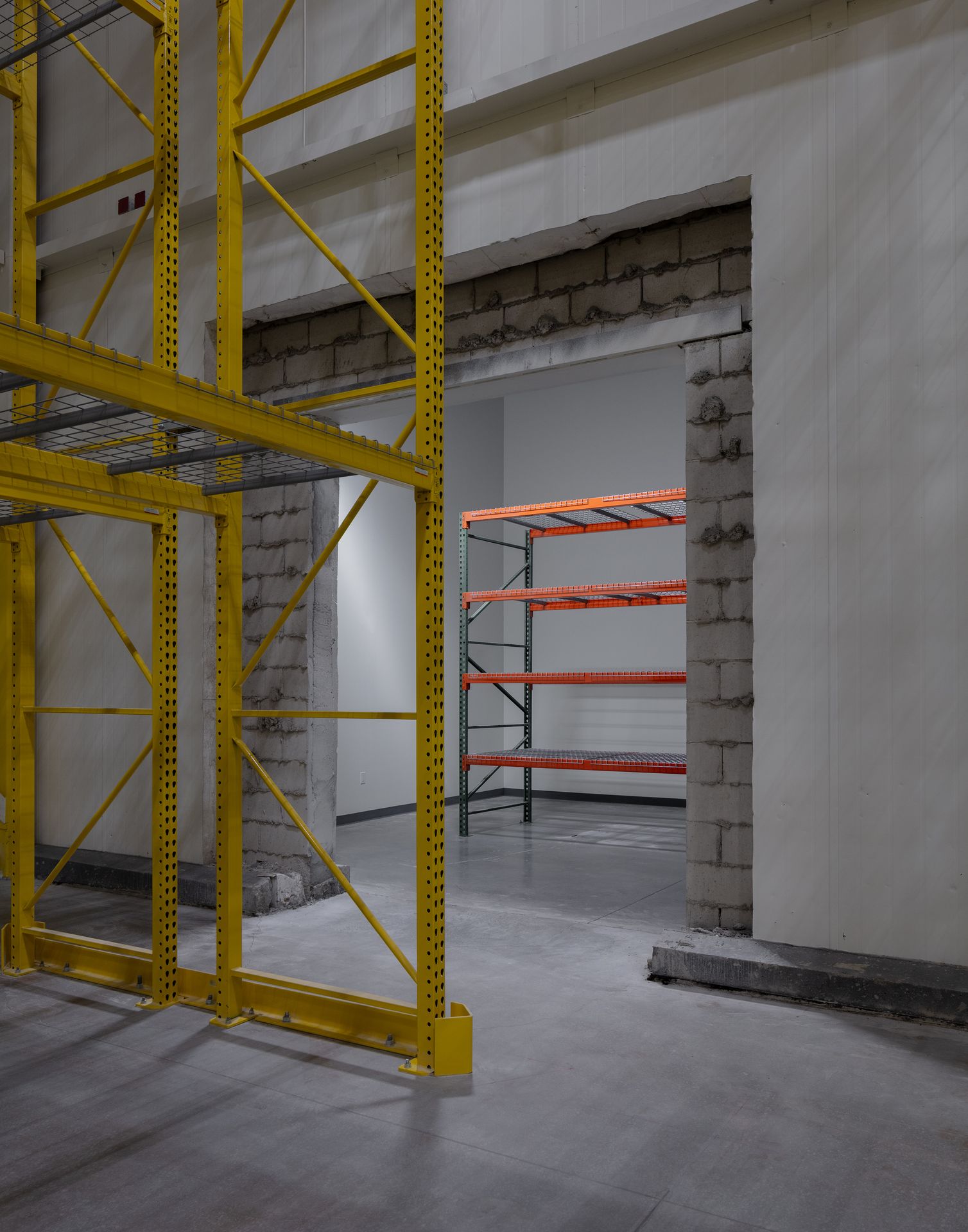 Industrial interior view looking into a post-construction direct-to-consumer fulfillment space, featuring a concrete block wall and yellow structural scaffolding.
