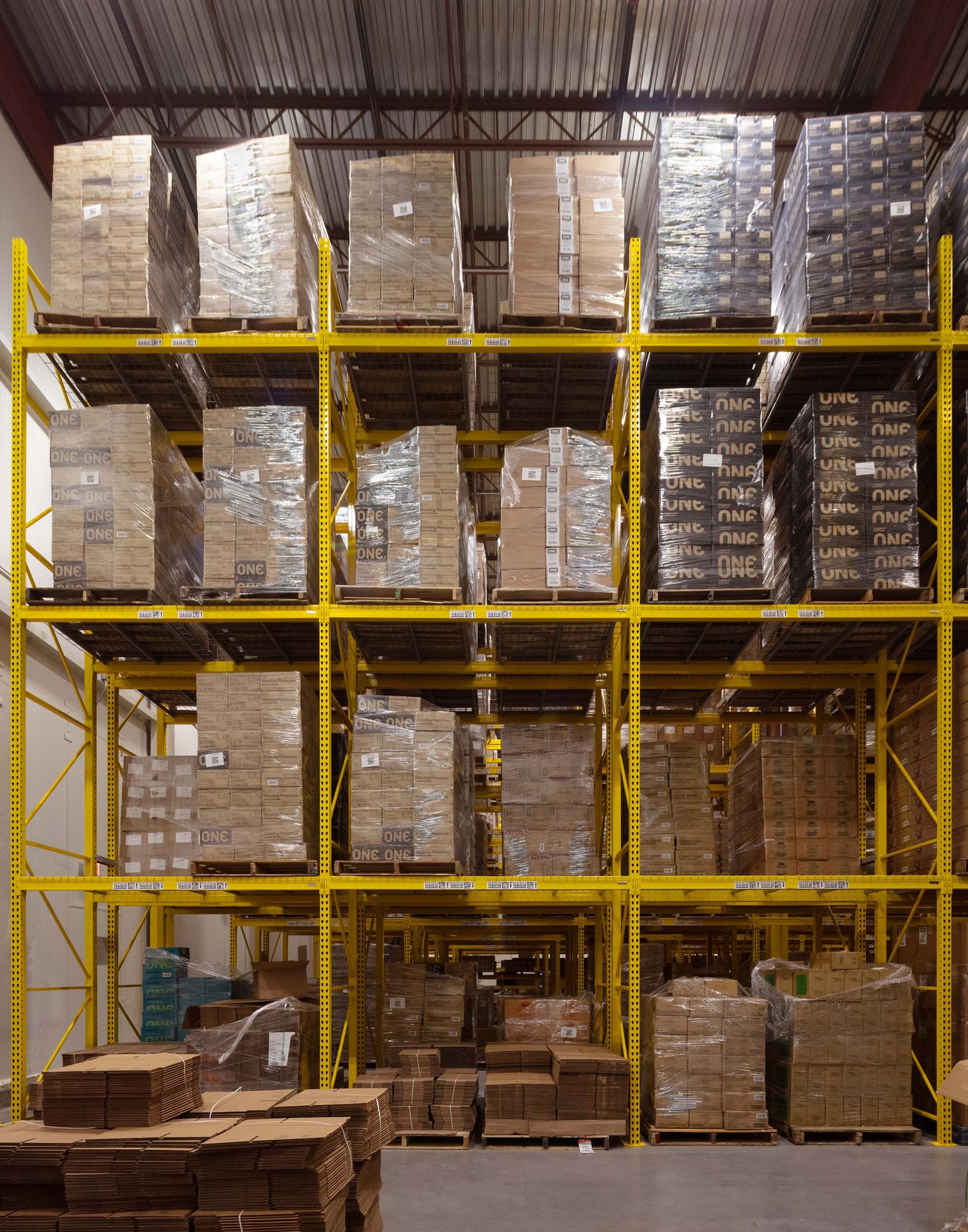 Looking through the high-density grid rows of tall yellow industrial warehouse shelving packed with inventory.