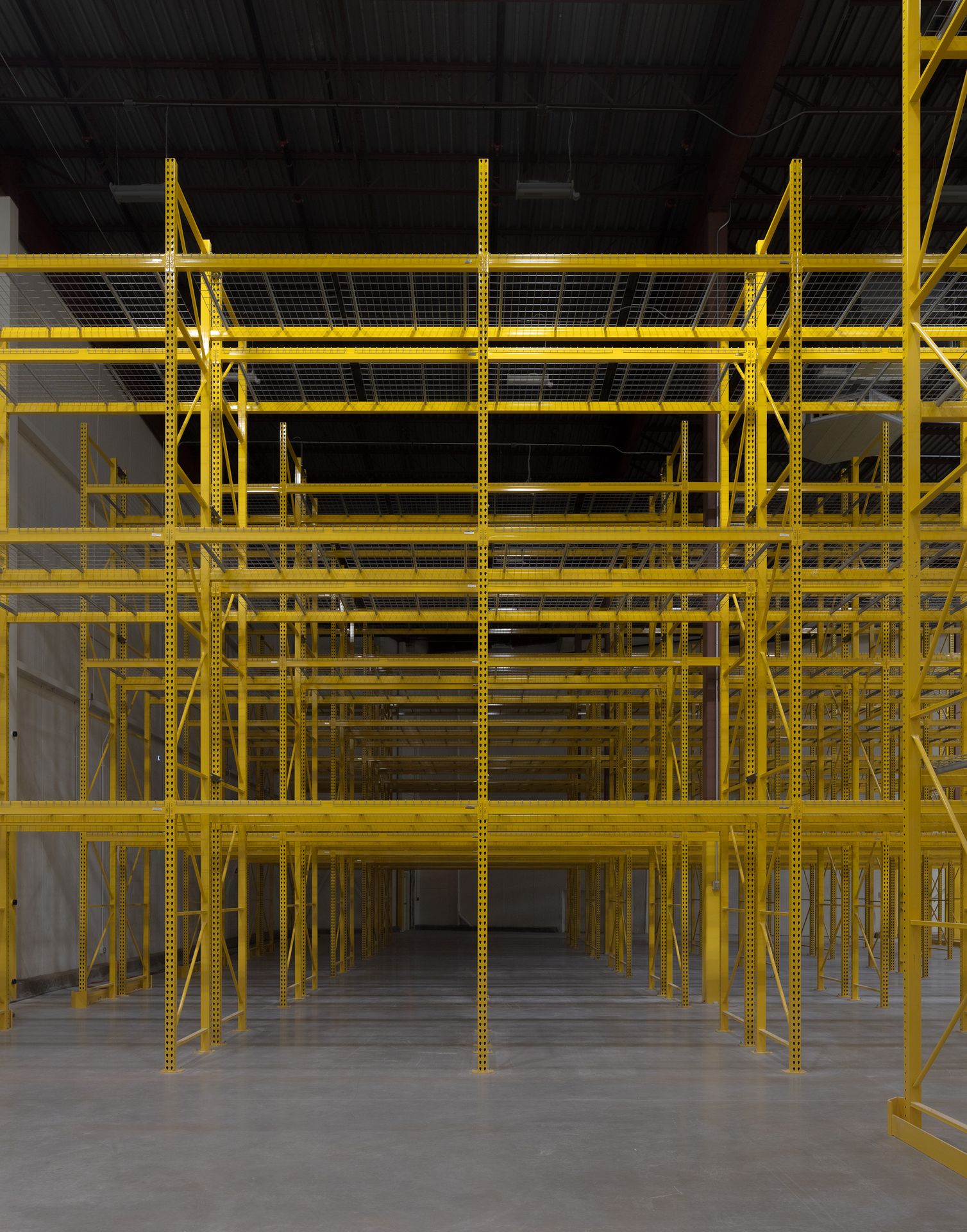 A massive industrial warehouse interior filled with a dense, sprawling network of yellow safety scaffolding or structural framing.